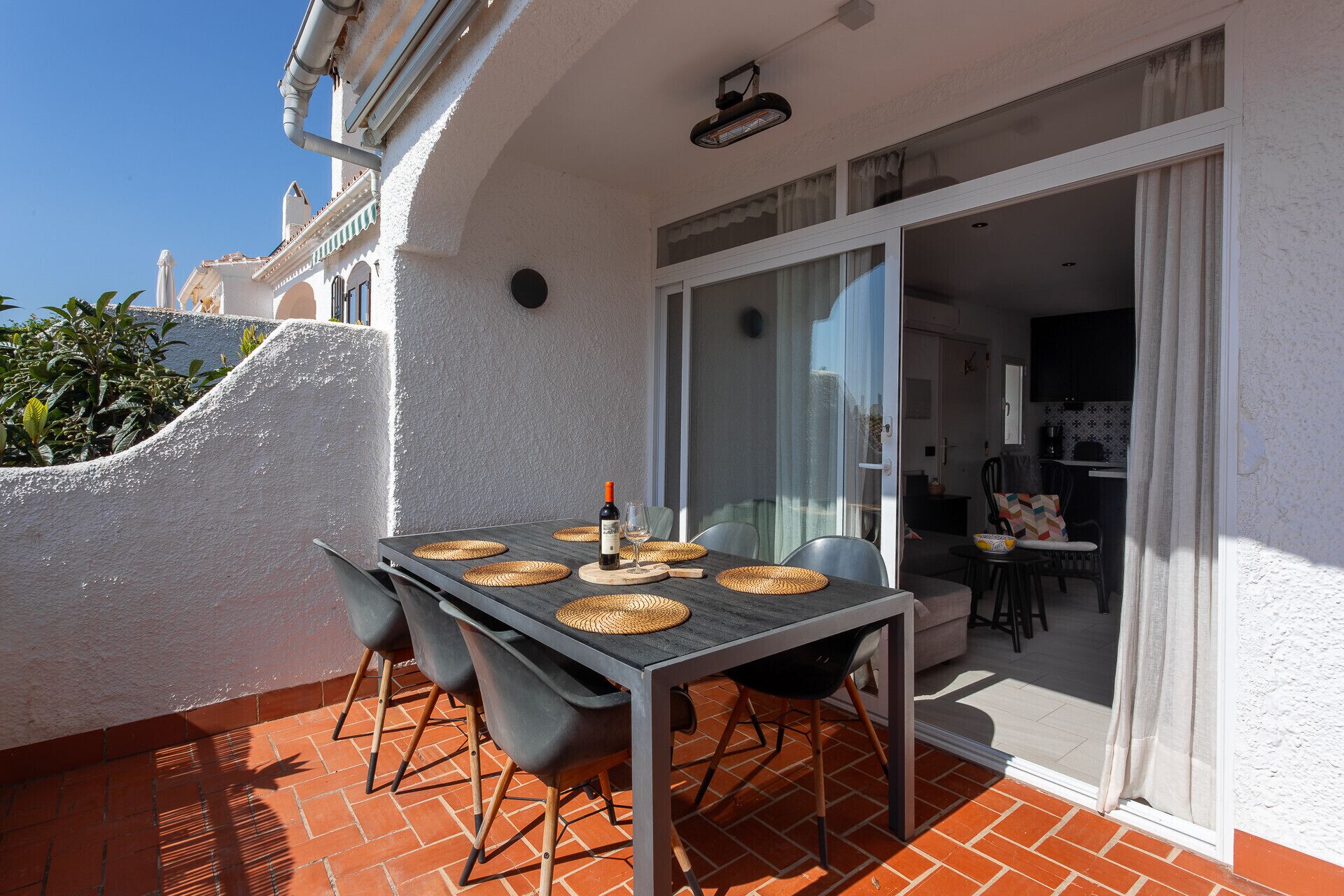 Un patio con una mesa preparada para dos personas, una silla y una botella de vino.