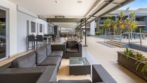 An outdoor seating area with sofas and tables, a covered walkway, and a view of the building's exterior. - Perfect for Two – Studio at the Esplanade (Urangan)
