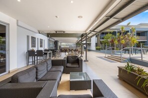 An outdoor seating area with sofas and tables, a covered walkway, and a view of the building's exterior. - Perfect for Two – Studio at the Esplanade (Urangan)