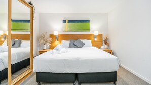 A hotel room with a large bed, two bedside tables, a mirror, and a painting on the wall. - Perfect for Two – Studio at the Esplanade (Urangan)