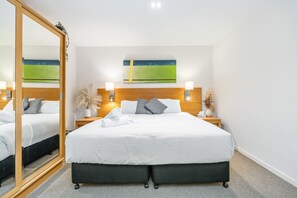 A hotel room with a large bed, two bedside tables, a mirror, and a painting on the wall. - Perfect for Two – Studio at the Esplanade (Urangan)
