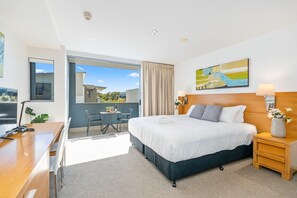 A hotel room with a bed, a desk, a chair, a small table, a nightstand, a lamp, and a painting. - Refreshed Esplanade Studio for Two (Urangan)