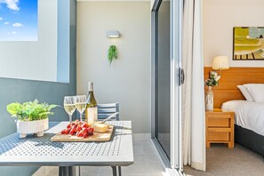 A balcony with a table set for a meal, a bottle of wine, and a plant. - Refreshed Esplanade Studio for Two (Urangan)