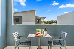A balcony with two chairs and a table set for a meal, featuring a bottle of wine, cheese, and fruits. - Refreshed Esplanade Studio for Two (Urangan)