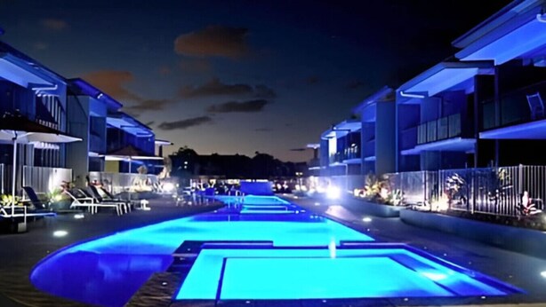 A nighttime swimming pool area with lounge chairs and umbrellas, surrounded by modern buildings. - Perfect for Two – Studio at the Esplanade (Urangan)