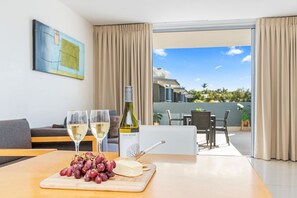 A room with a dining table set with two glasses of white wine, a bottle of wine, a cheese board with grapes, and a laptop.