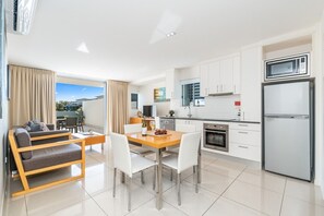 A modern kitchen with white cabinets, a stainless steel refrigerator, and a dining area with a wooden table and white chairs.