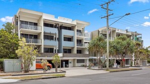 A multi-story building with balconies, a parking area, and a clear sky. - Relaxed Esplanade Living near Pier & Marina (Urangan)