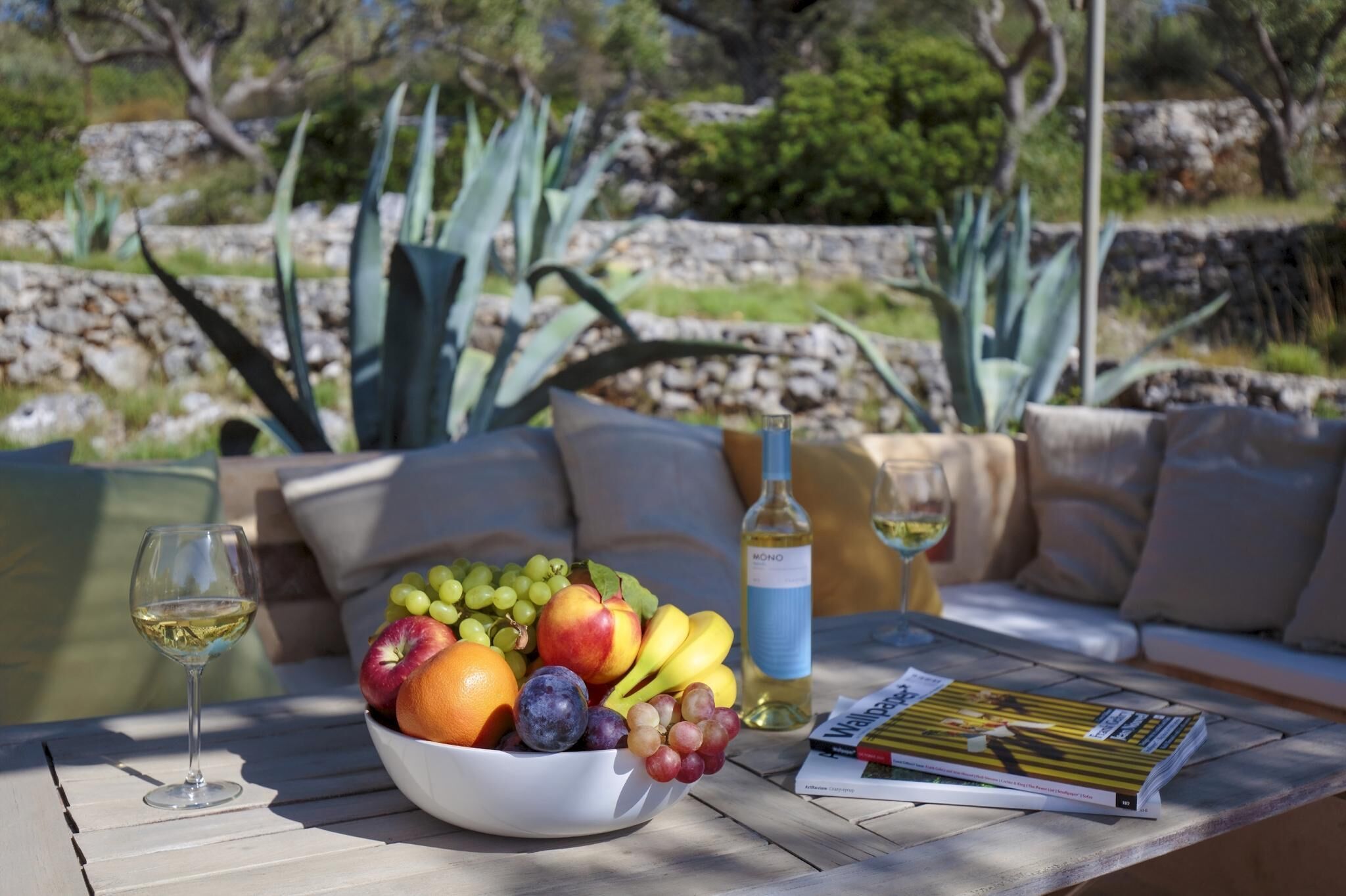 A table with a bowl of fruit, a bottle of wine, and a magazine.