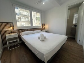A bedroom with a large bed, a bedside table, a nightstand, a window with a view of buildings, and a mirror. - Your getaway on the Fuengirola Promenade (Fuengirola)