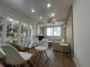 A modern living room with a glass dining table, white chairs, a beige sofa, and a ceiling fan. - Your getaway on the Fuengirola Promenade (Fuengirola)