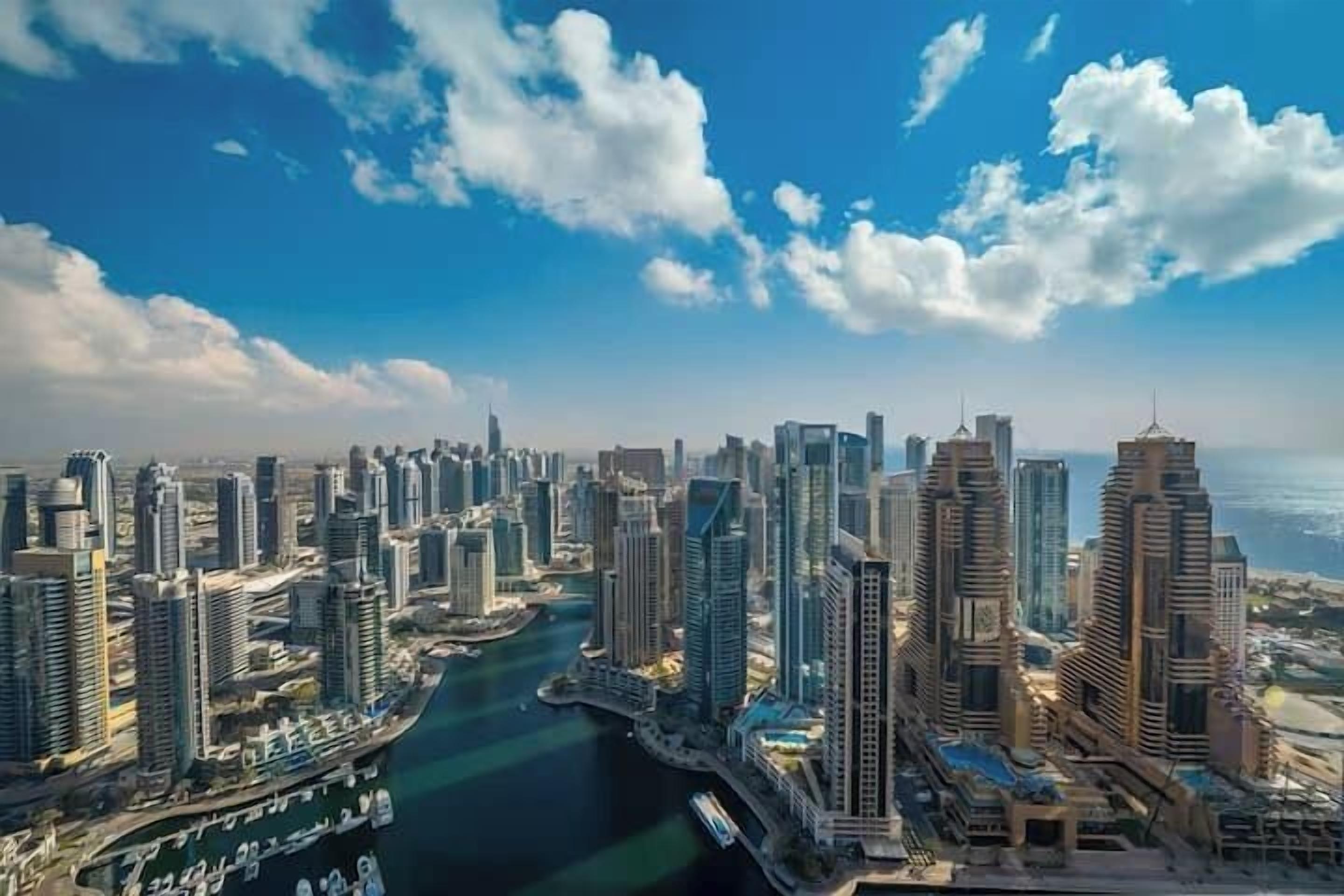 A coastal cityscape with modern high-rise buildings, a marina, and a clear blue sky.