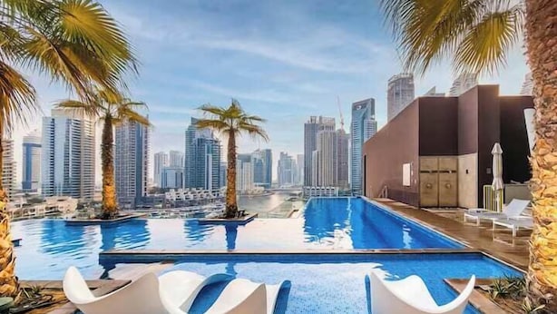 Una piscina con sedie moderne, palme e uno skyline urbano sullo sfondo.