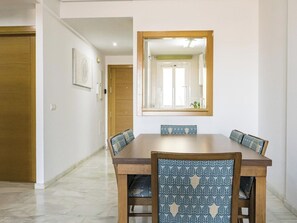 Un coin repas comprenant une table rectangulaire, quatre chaises dotées de coussins à motifs et un grand miroir placé au-dessus de la table.