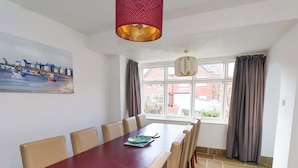 A dining area with a long table, multiple chairs, a painting on the wall, and a view through the window. - 11 Peasholm Avenue (Scarborough)