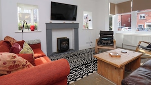 A living room with a fireplace, a sofa, a chair, a coffee table, and a TV mounted on the wall. - 11 Peasholm Avenue (Scarborough)