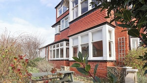 A two-story brick house with a red roof, white-framed windows, and a wooden bench in the garden. - 11 Peasholm Avenue (Scarborough)
