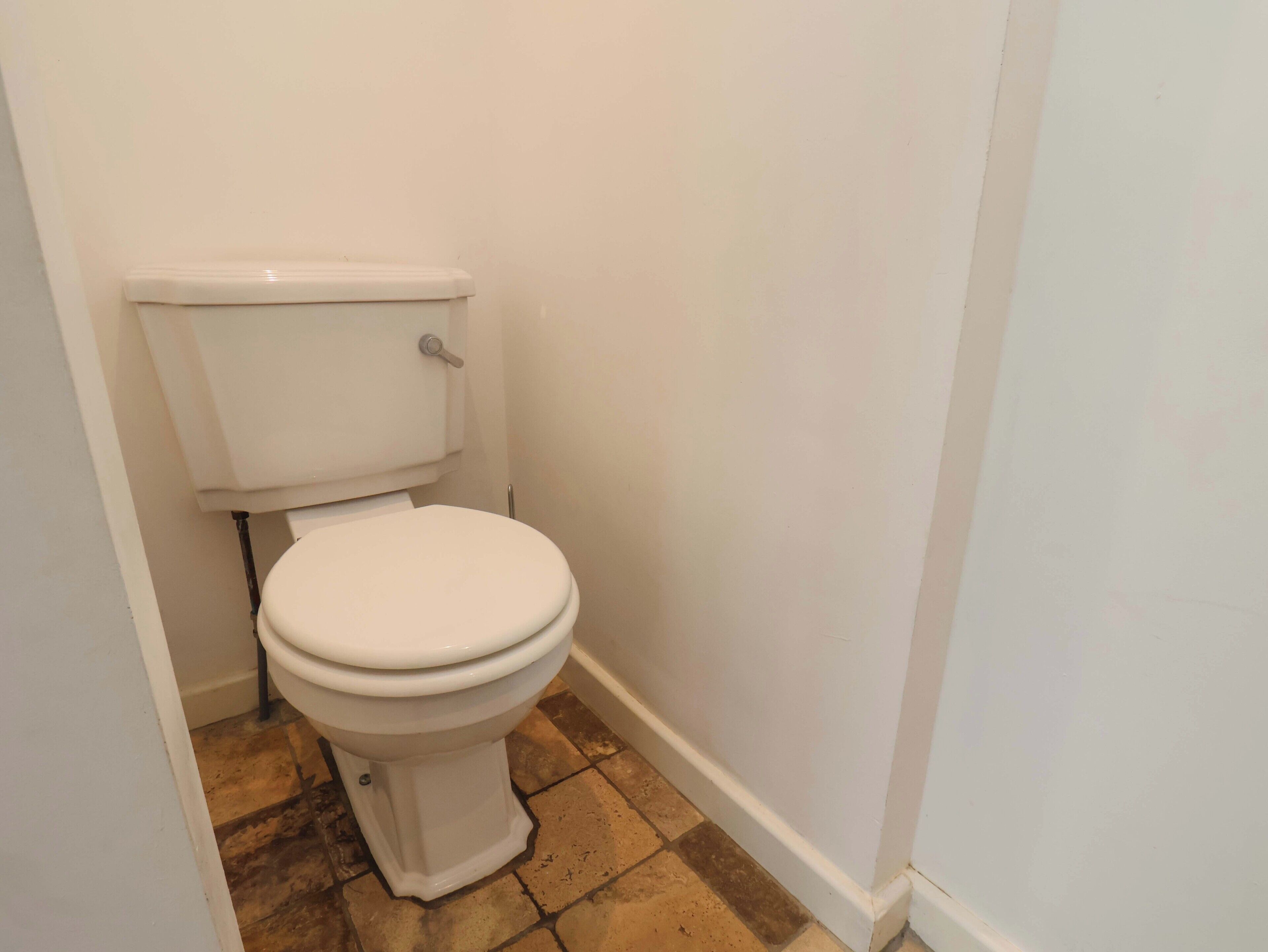 A white toilet in a narrow bathroom with tiled flooring.