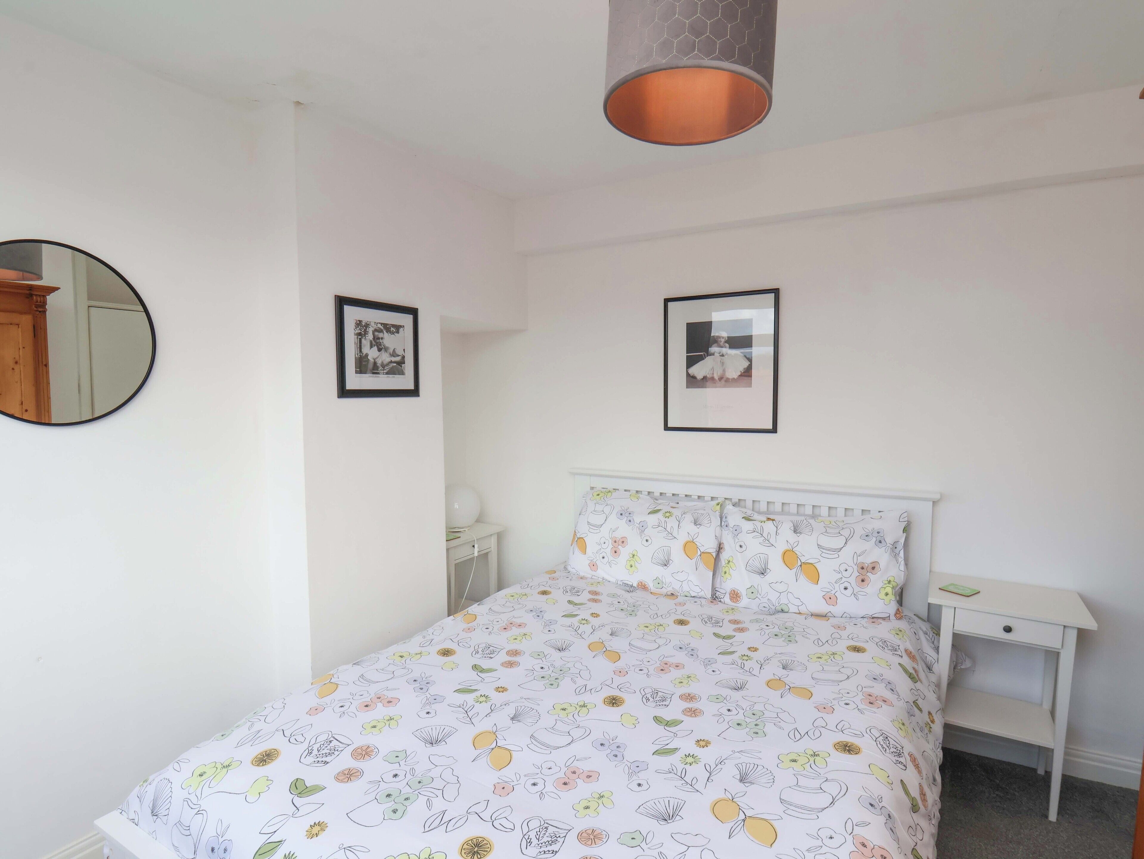A bedroom with a bed, a nightstand, a mirror, and two framed pictures on the wall.
