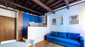 A living area with a blue sofa, a dining table with chairs, and a kitchen area with blue cabinets. - Welcome in Trastevere apartment (Roma)