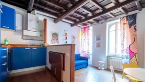 A compact kitchen with blue cabinets, a wooden ceiling, and a dining area with a white table and chairs. - Welcome in Trastevere apartment (Roma)