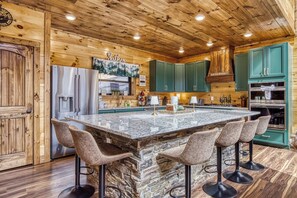 A kitchen with a large island, green cabinets, and a stainless steel refrigerator. - Longview Lodge - Mountain Views, Hot Tub, Game Room (Gatlinburg)