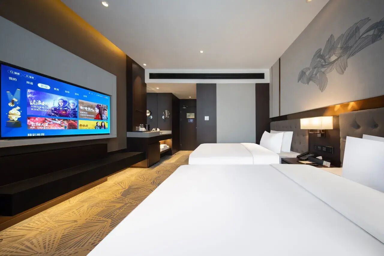 Een moderne hotelkamer met een groot flatscreen televisietoestel, een bed, een nachtkastje en een wandlamp.