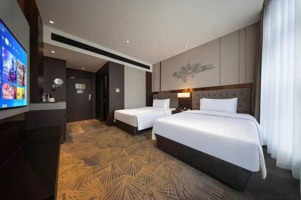 Ein Hotelzimmer mit zwei Betten, einem Fernseher, einem Wandbild und einem gemusterten Teppich.