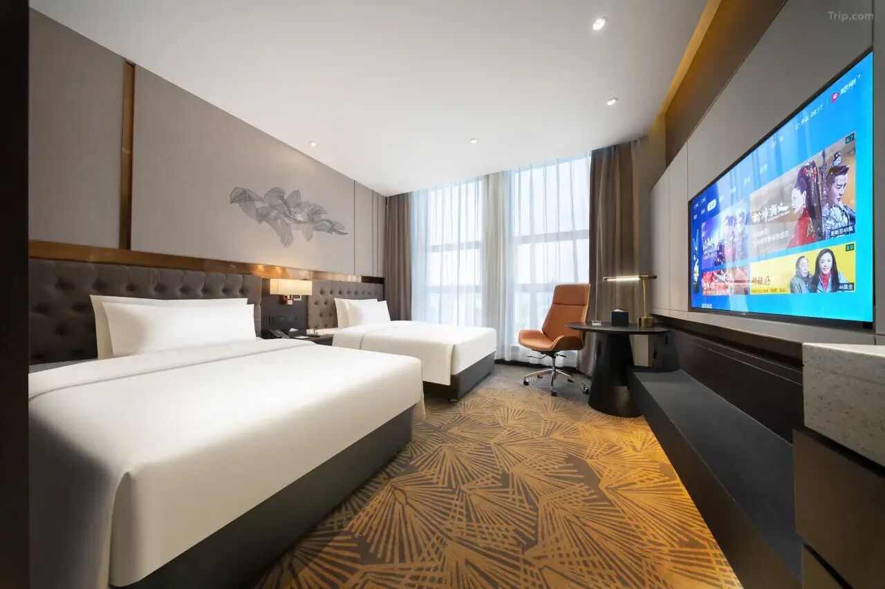 A hotel room with two beds, a TV, a desk, and a large window.