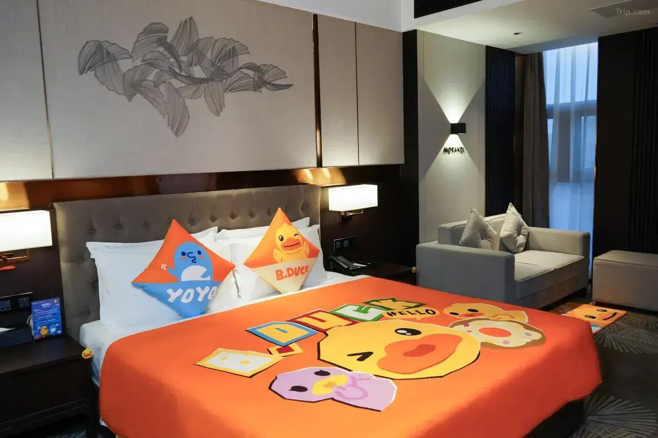 A hotel room with a bed, a sofa, a nightstand, a wall-mounted lamp, and a window with curtains.