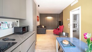 Een moderne keuken met een magnetron, een eethoek met tafel en stoelen, een rode fauteuil en een tv aan de muur.