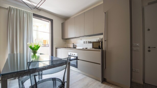 Een moderne keuken met een glazen eettafel, roestvrijstalen apparatuur en uitzicht op de omgeving.