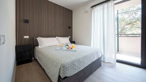 Een moderne slaapkamer met een groot bed, een nachtkastje, een dienblad met ontbijtartikelen en uitzicht op de omgeving door een groot raam.