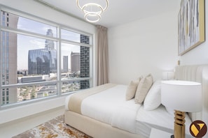 A modern bedroom with a large window, a bed, a bedside lamp, and a view of city buildings. - Vogue | The Lofts near Burj Khalifa | Dubai Mall (Dubai)