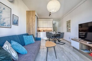 A modern living room with a sofa, a dining table, and chairs. There is a kitchen in the background, a television, and artwork on the walls. - Sofia`s Designer Apartment (St. Julian`s)