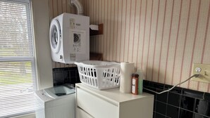 A laundry area with a washing machine, a dryer, a white cabinet, a laundry basket, and a wall-mounted vent. - Bright Studio Near Boston — Transit Access — Washer/Dryer (Malden)