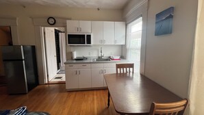 A compact kitchen with white cabinets, a microwave, a sink, and a dining table with chairs. - Bright Studio Near Boston — Transit Access — Washer/Dryer (Malden)