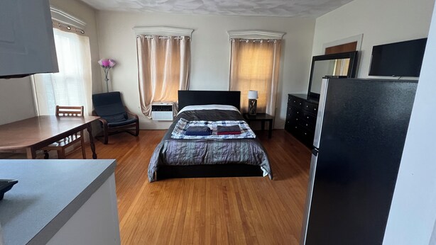 A hotel room with a bed, a desk, a chair, a dresser, and a television. - Bright Studio Near Boston — Transit Access — Washer/Dryer (Malden)