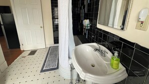 A bathroom with a white sink, a mirror, black tiled walls, a white door, and a black tiled floor. - Bright Studio Near Boston — Transit Access — Washer/Dryer (Malden)