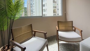 A room with two wooden chairs, a potted plant, and a large window with a view of tall buildings. - Your refuge in Guarujá, just steps from the beach! BRA (Guarujá)