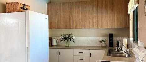 Eine Küche mit weißen Geräten, Holzschränken, einem Deckenventilator und einem gefliesten Boden.