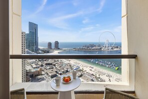 Un balcon avec une table, une vue sur une plage, une grande roue et des immeubles de grande hauteur.