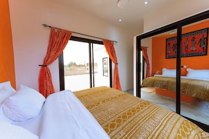 Habitación de hotel con dos camas, cortinas naranjas, un ventanal grande y un mural en la pared.