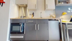A modern kitchen with grey cabinets, a microwave, a dishwasher, and a small countertop area with a kettle and a yellow lamp. - Student Only Highbury (London)