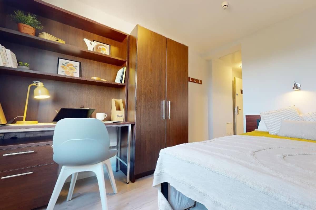 Une chambre à coucher comprenant un lit, une table de chevet, une lampe, une chaise et une armoire.