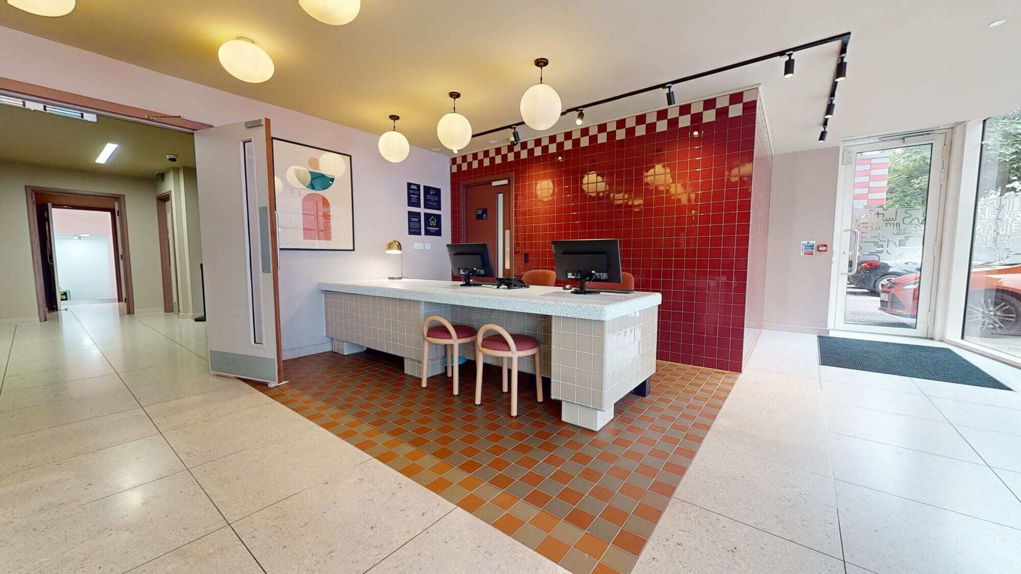 A reception area with a checkered floor, a reception desk with two chairs, and a red tiled wall.