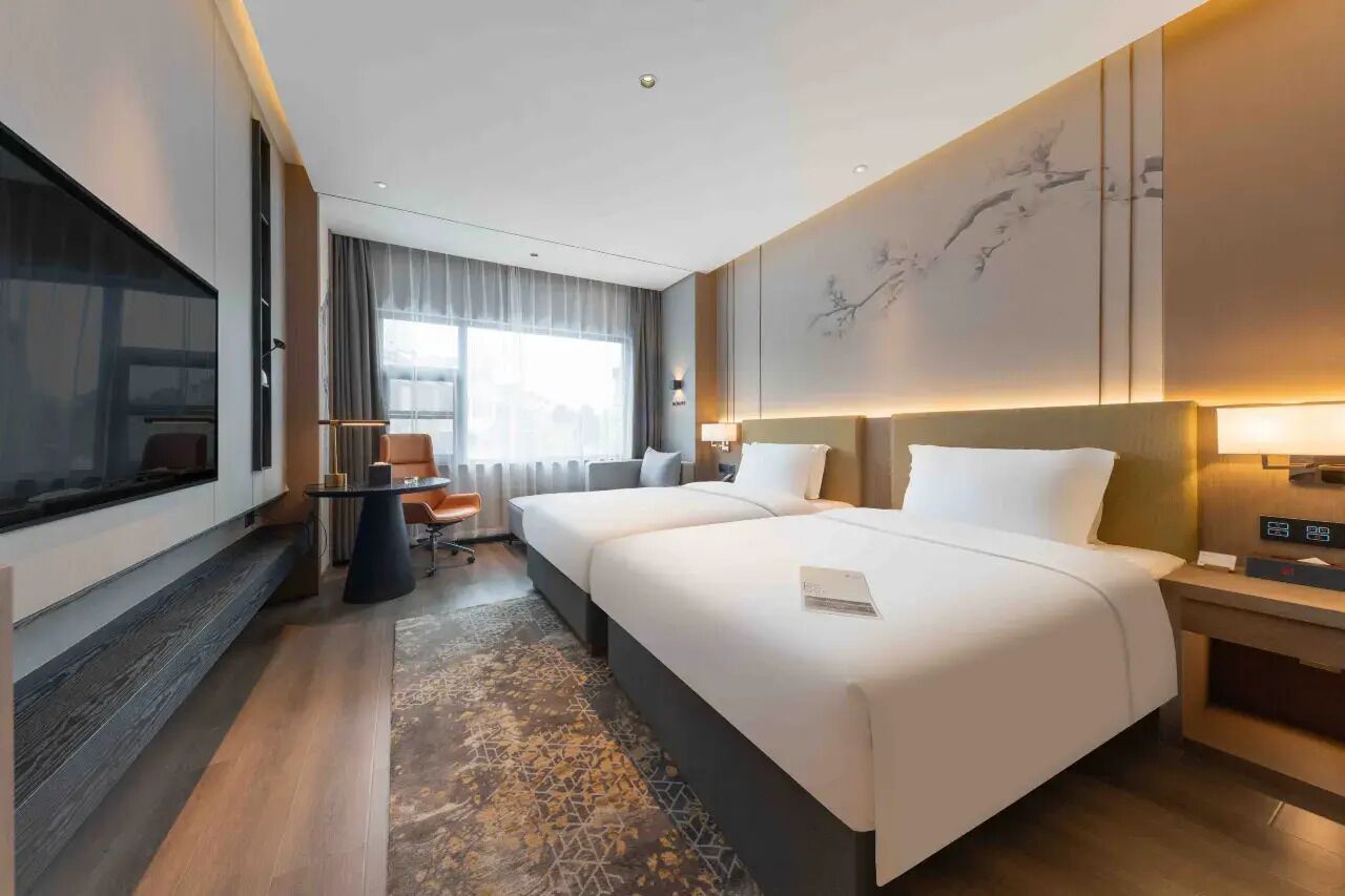Habitación de hotel con una cama grande, un escritorio, una silla, un televisor y vistas a la ciudad.