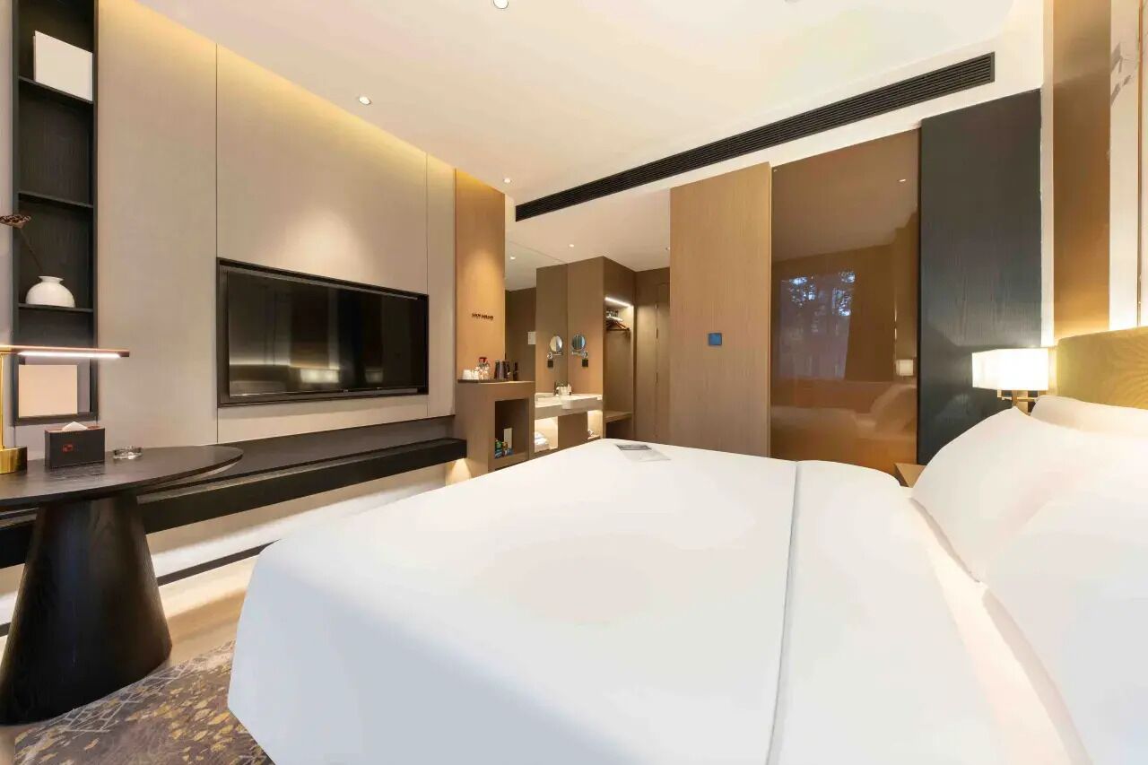 Ein modernes Hotelzimmer mit einem großen Bett, einem Flachbildfernseher, einem Schreibtisch mit Lampe und einem Spiegel.