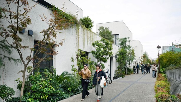 Um caminho ladeado por edifícios modernos com áreas verdes, uma bicicleta e pedestres.