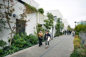 Un chemin bordé de bâtiments modernes, agrémenté de verdure, où l’on croise des cyclistes et des piétons.